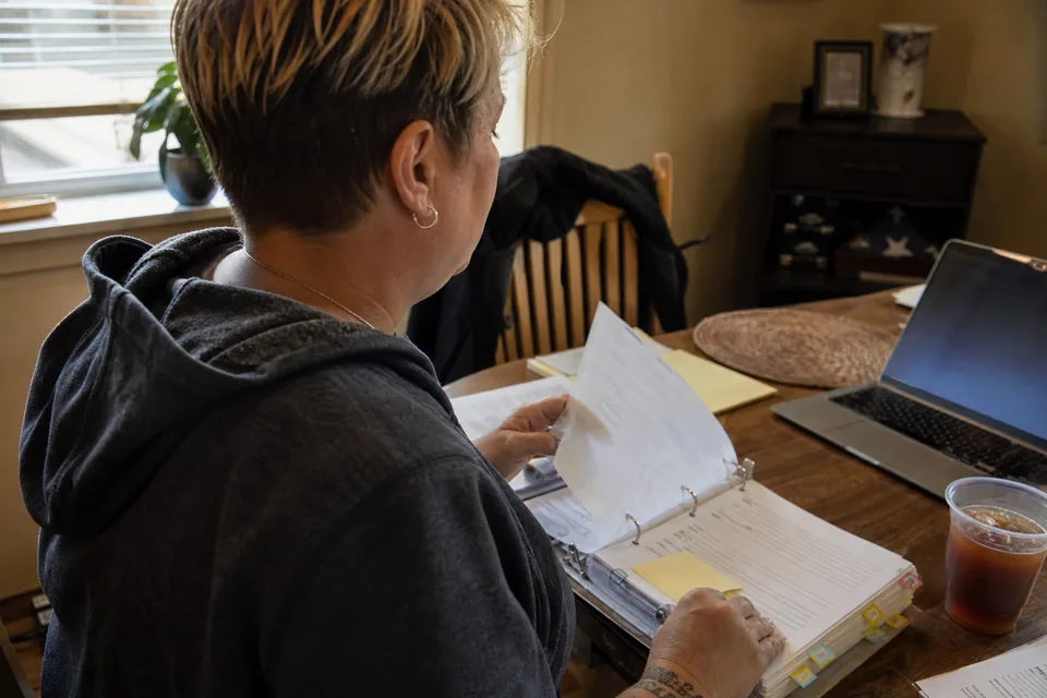 A veteran at a dining table turning pages in a binder of service treatment records next to a laptop
