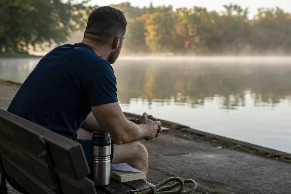 A veteran sitting on a lakeside bench in the early morning mist with a thermos beside him