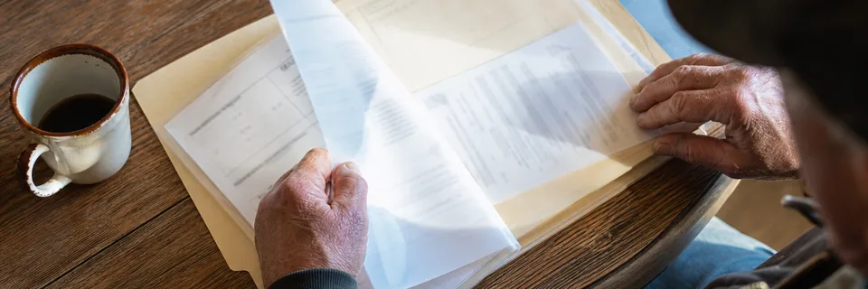 Hands of a veteran spreading printed medical records and a thick folder across a kitchen table