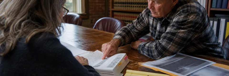 A veteran and an accredited attorney going through a binder of service medical records at a law office conference table