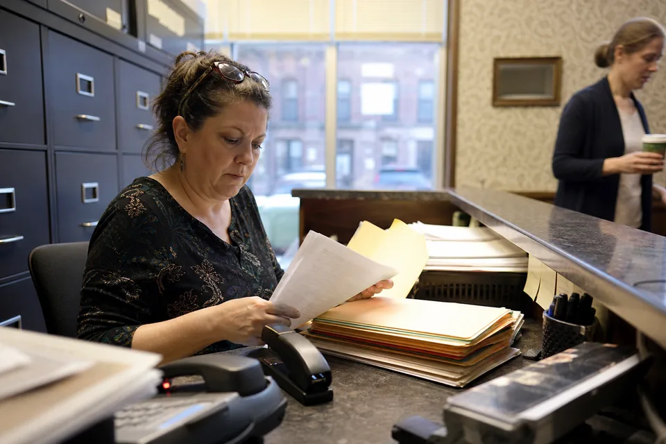 An intake paralegal at a small law practice sorting printed veteran request forms at a front desk